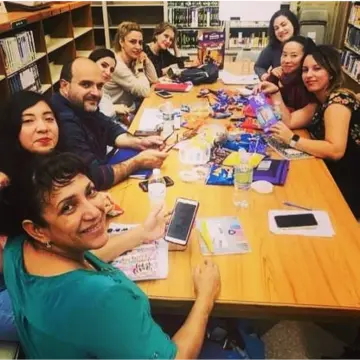 Maria and her students sitting around a table, engaged in a lively speaking class discussion.