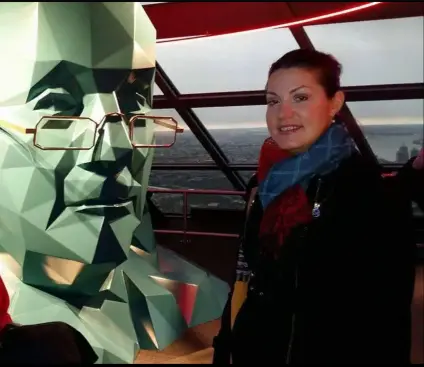 Maria is standing next to a statue, symbolizing learning and academic growth.